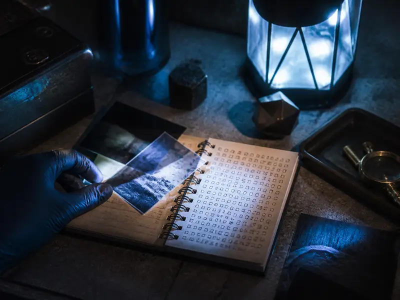 Closeup detective evidence photographs cipher notebook under blue lamplight