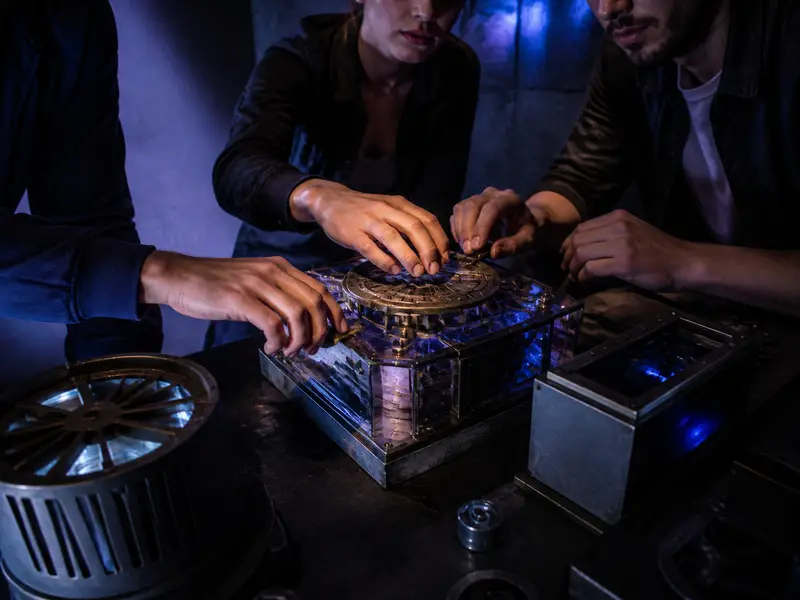 Friends hands collaborating on mechanical escape room puzzle tabletop